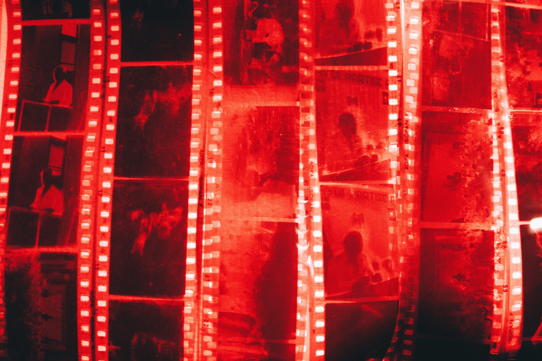 Strips of old black-and-white film negatives glow red on a light table, sprocket holes shining.